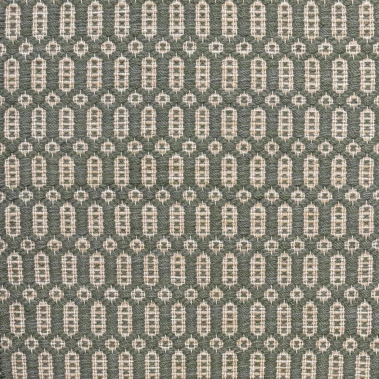 Handwoven wool rug with an oval and diamond lattice pattern in shades of sage green and beige. 