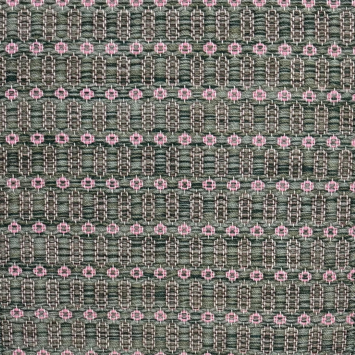 Handwoven wool rug with an oval and diamond lattice pattern in shades of green and brown with pink accents. 