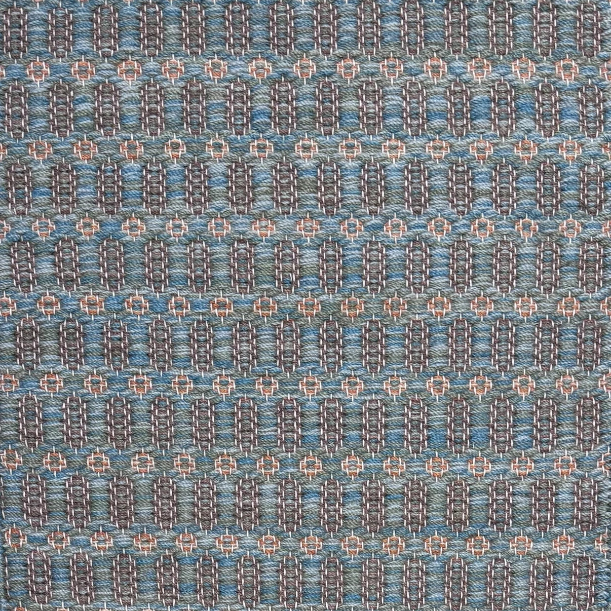 Handwoven wool rug with an oval and diamond lattice pattern in shades of blue and brown with clay pink accents.