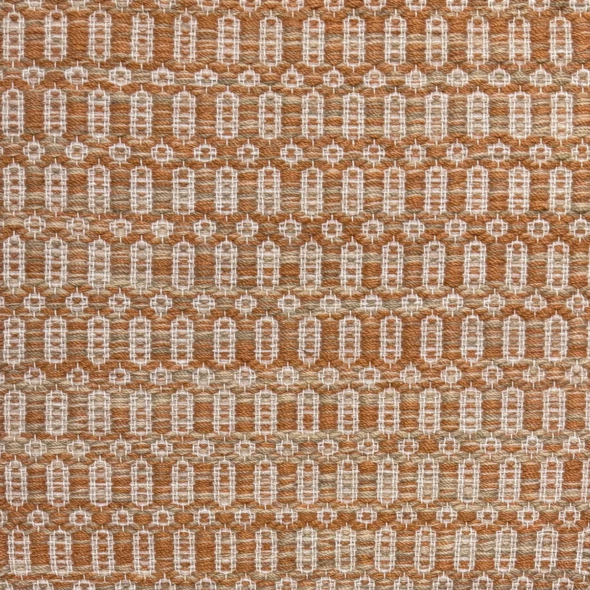 Handwoven wool rug with an oval and diamond lattice pattern in shades of orange and tan. 