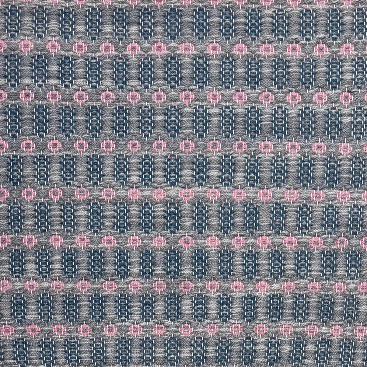 Handwoven wool rug with an oval and diamond lattice pattern in shades of grey and dark blue with pink accents.