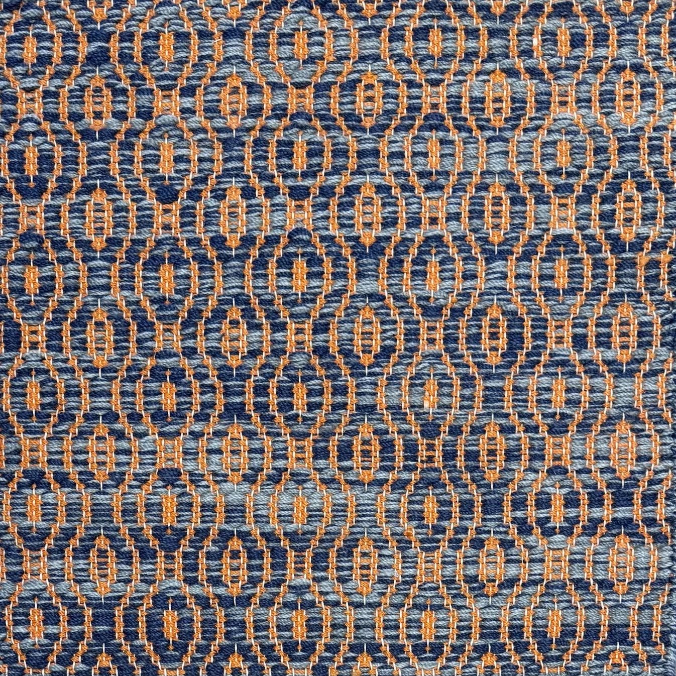 Handwoven wool rug with undulating oval stripe in shades of blue on an orange field. 