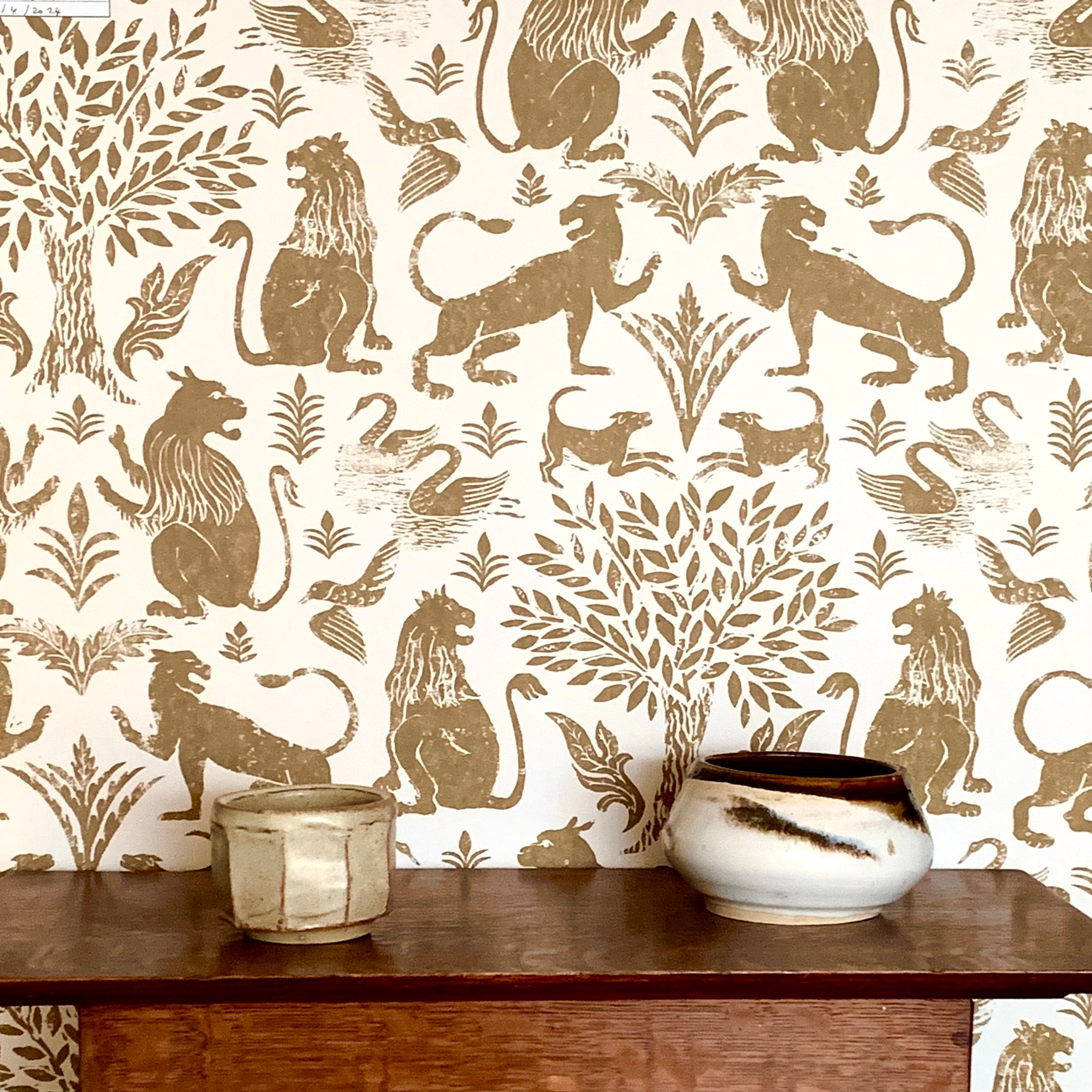 Detail of wallpaper in a lion and plant print in brown on a white field with  wooden table and ceramic vessels. 