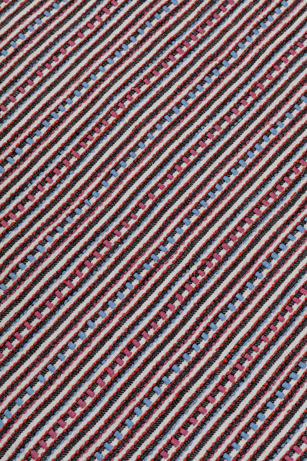 Detail of a dimensional embroidered fabric in an irregular stripe pattern in shades of gray, white, pink and blue.