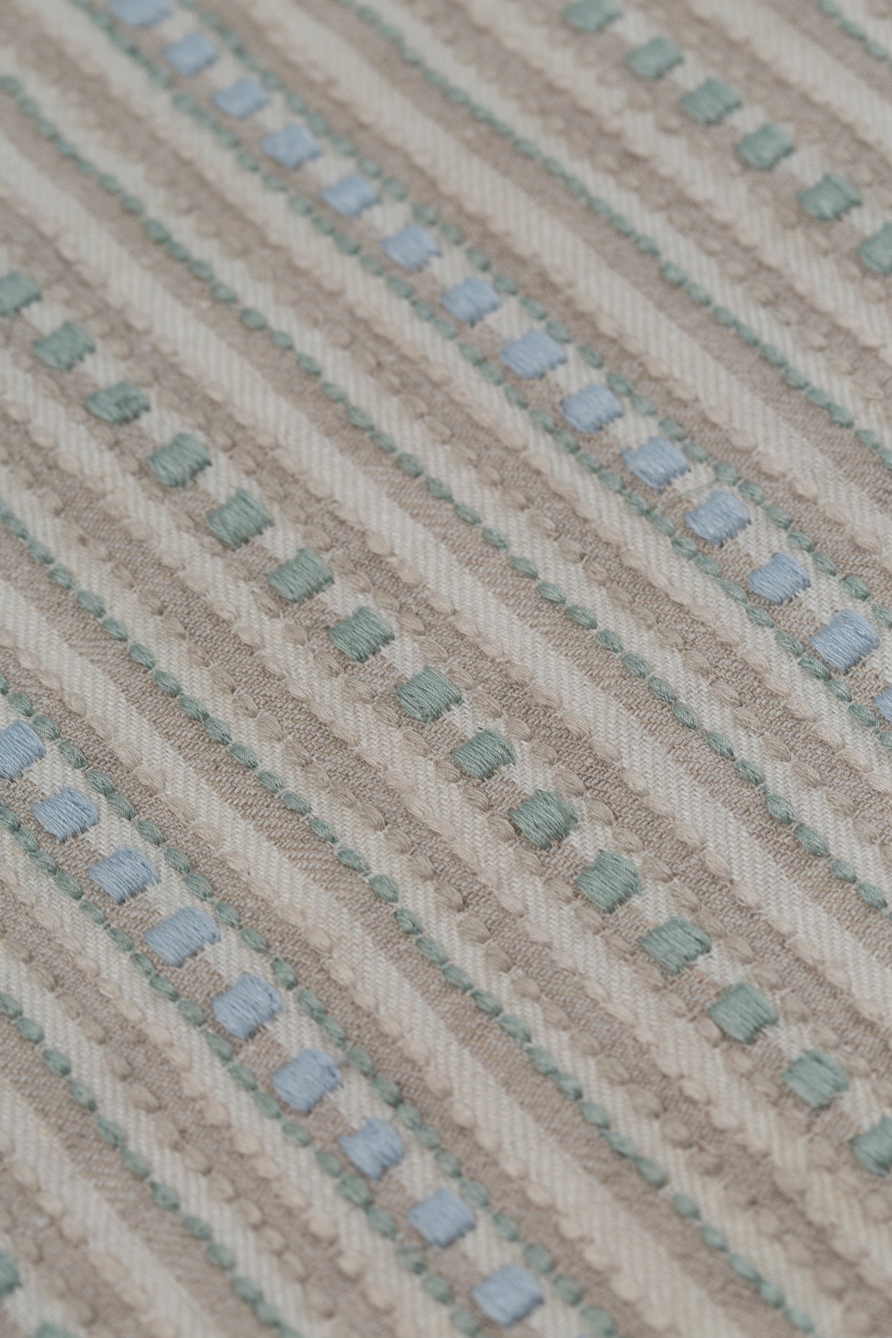 Detail of a dimensional embroidered fabric in an irregular stripe pattern in shades of taupe, cream, sage green and pale blue.