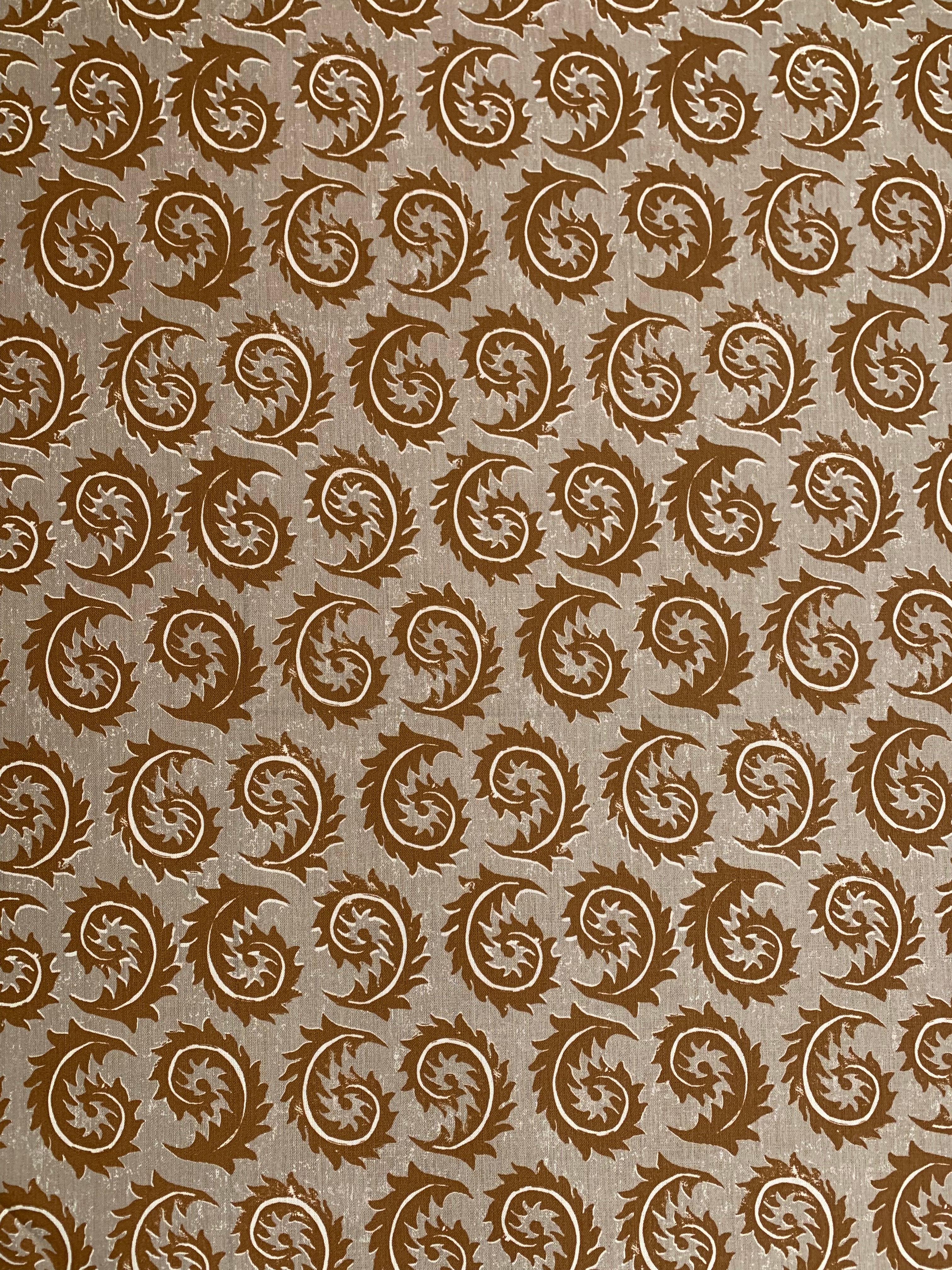 Detail of fabric in a repeating curved leaf print in white and brown on a tan field.