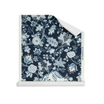 Roll of wallpaper in scrolling floral vine pattern in shades of blue and white on navy blue.