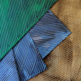 Pile of wallpaper swatches with dimensional combed patterns in indigo, emerald and tan colorways.