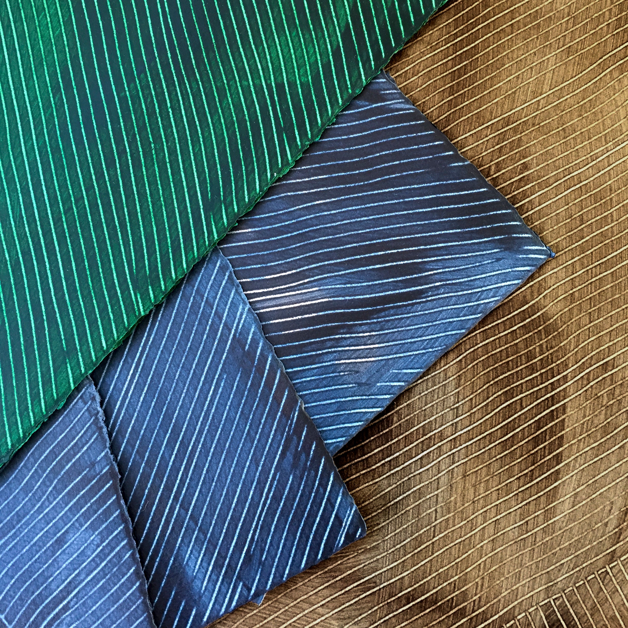 Pile of wallpaper swatches with dimensional combed patterns in indigo, emerald and tan colorways.