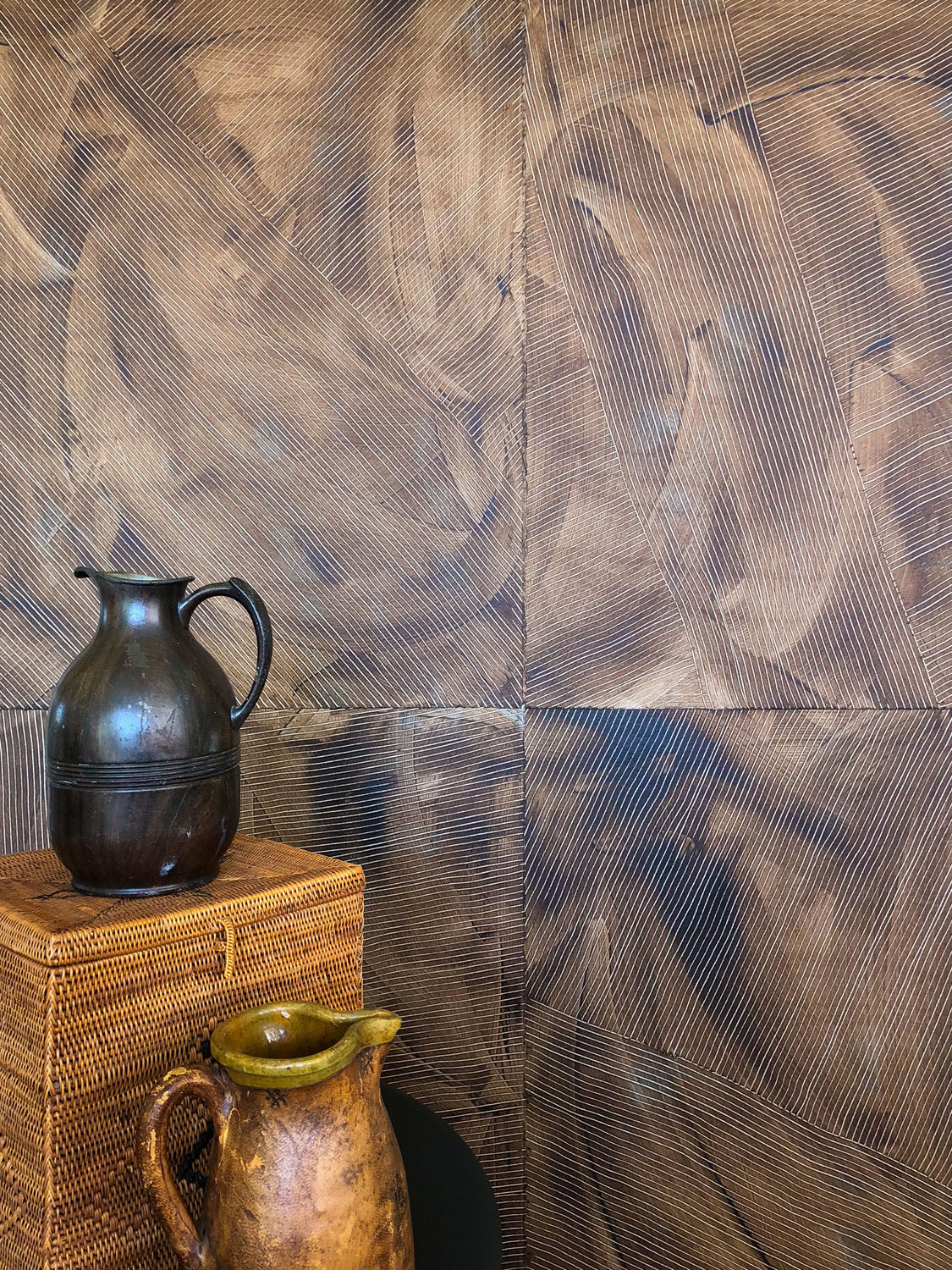 Vases stacked in front of a wall covered in multi-directional combed wallpaper in mottled brown.