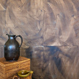 Vases stacked in front of a wall covered in multi-directional combed wallpaper in mottled brown.
