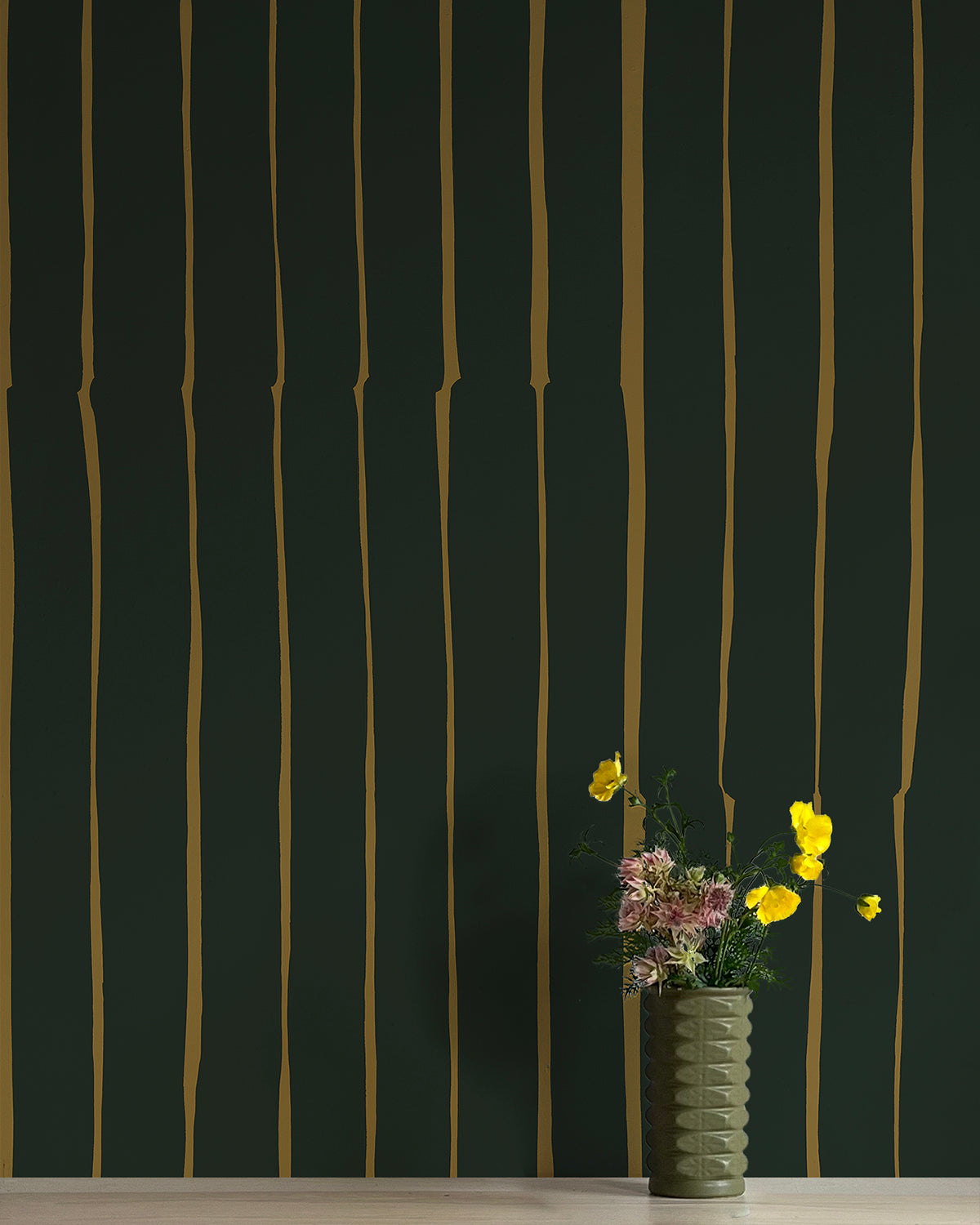 A vase of flowers stands in front of a wall covered in a playful irregular stripe print in mustard on a black field.