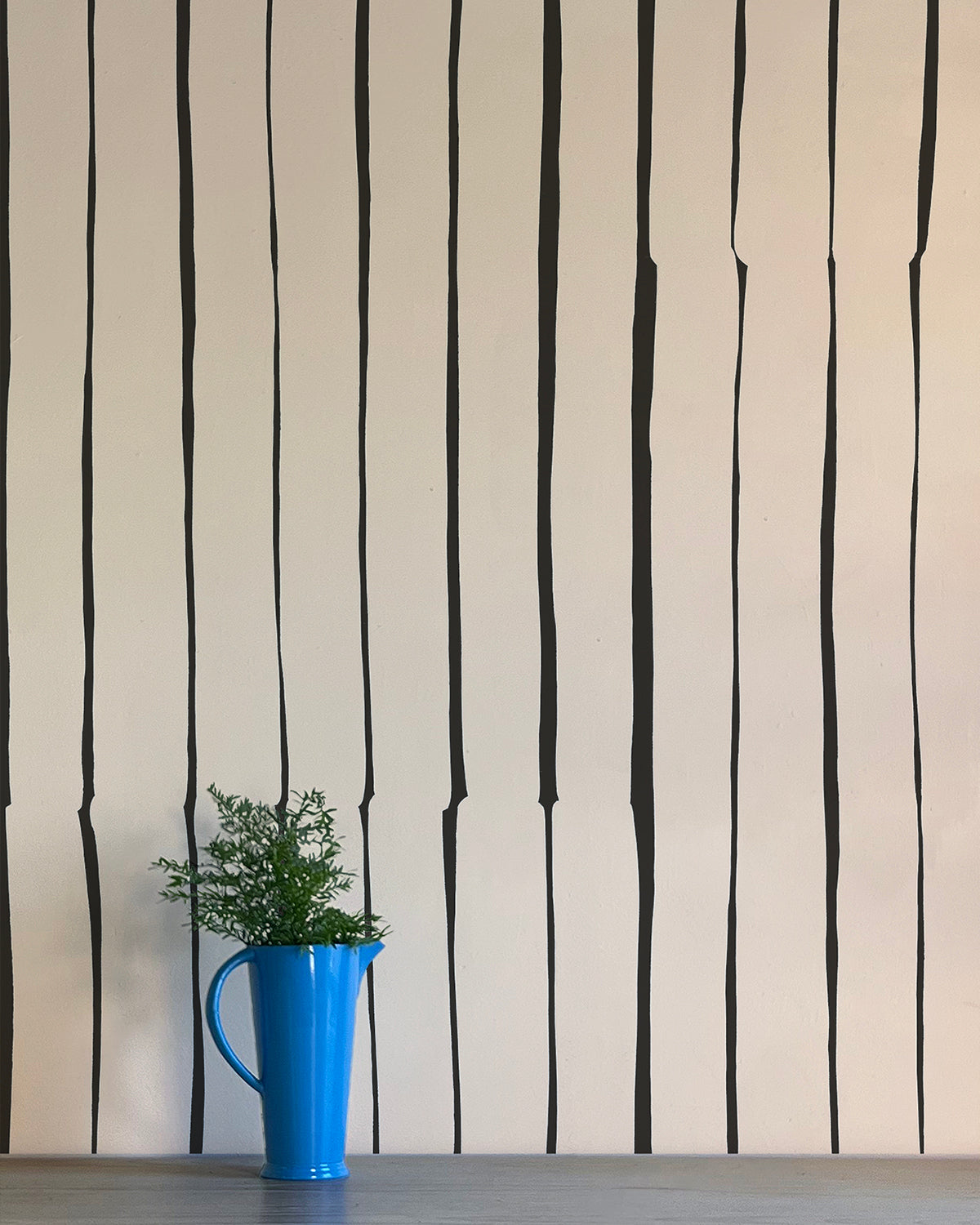 A vase of flowers stands in front of a wall covered in a playful irregular stripe print in black on a cream field.