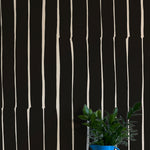 A vase of flowers stands in front of a wall covered in a playful irregular stripe print in cream on a black field.