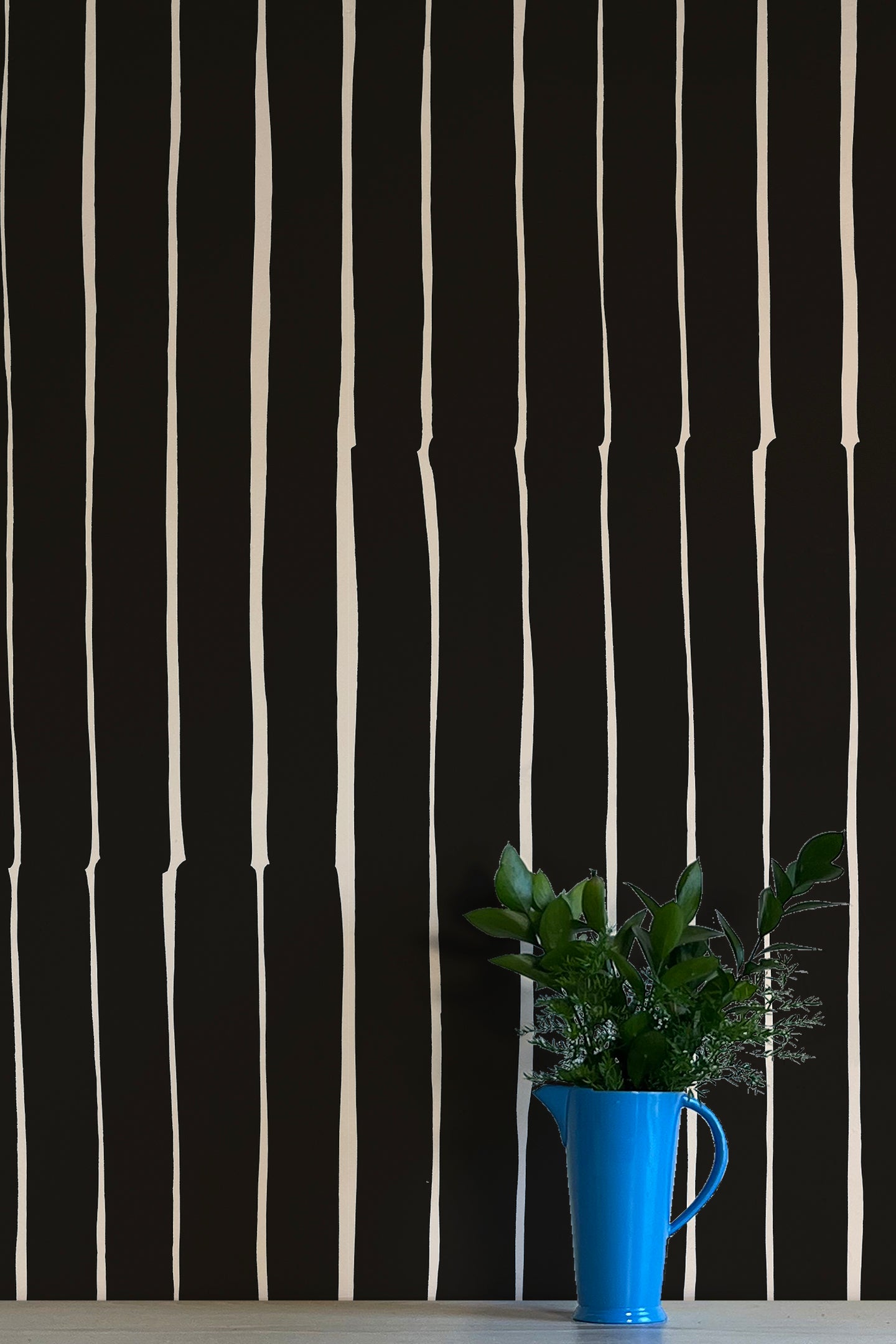 A vase of flowers stands in front of a wall covered in a playful irregular stripe print in cream on a black field.