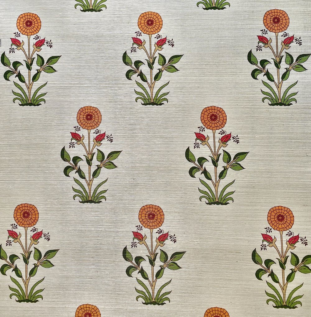 Detail of fabric in a large-scale marigold print in orange, red and green on a tan field.