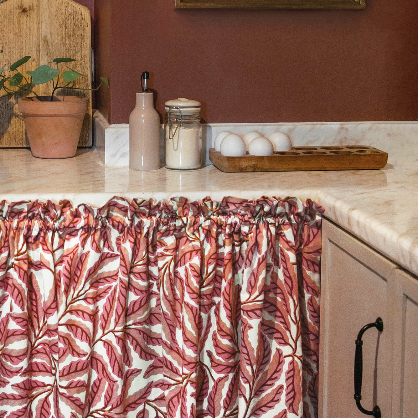 Kitchen with pink leaf-patterned curtain, countertop items, and a painting on the wall.