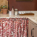 Kitchen with pink leaf-patterned curtain, countertop items, and a painting on the wall.
