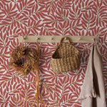 Wall with pink leaf-patterned wallpaper featuring a wooden hook with decorative items.