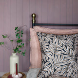 Bedroom with pale purple walls, floral-patterned pillow, and small round table with a vase and books.