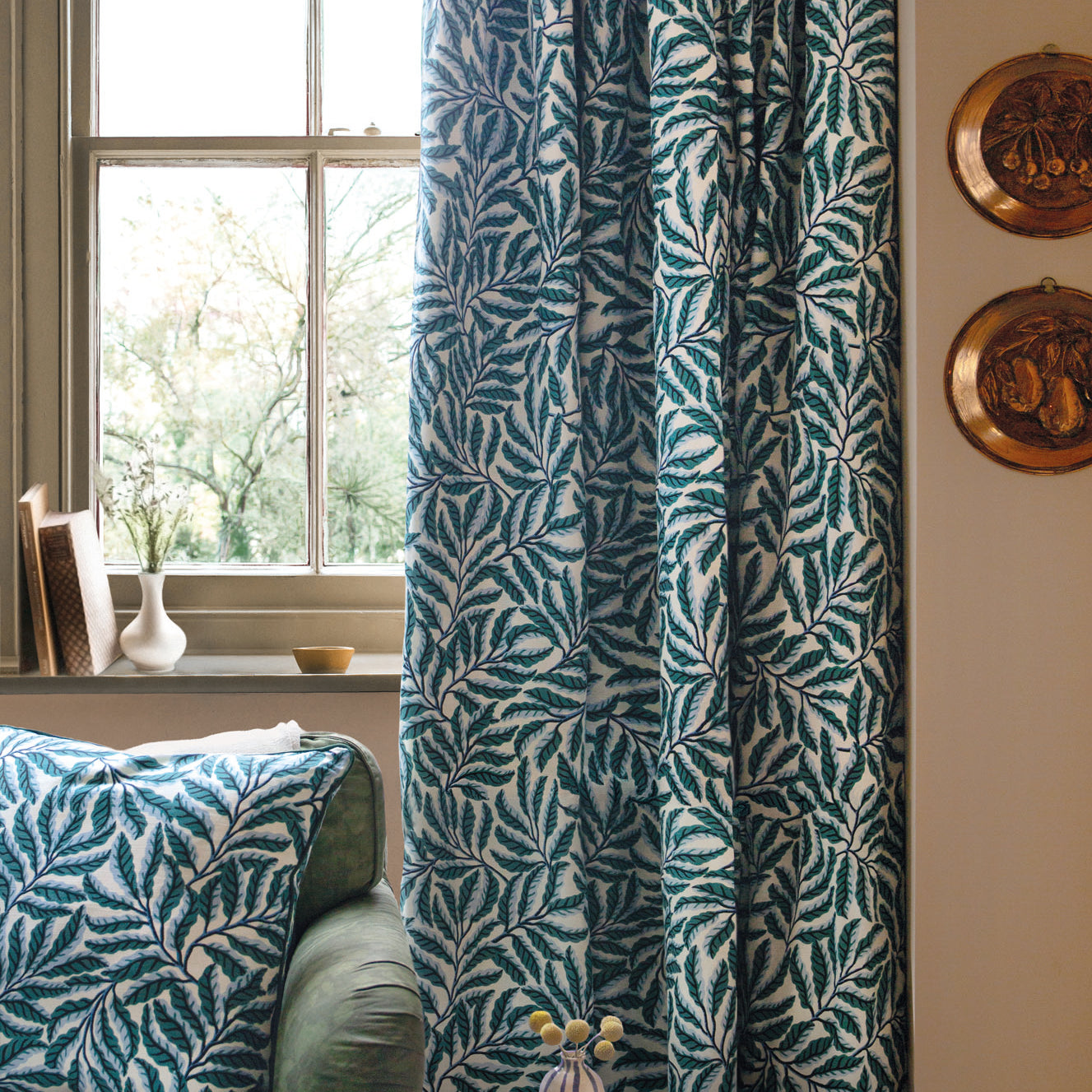 Green leaf-patterned curtain in a room with a couch and decorative items.