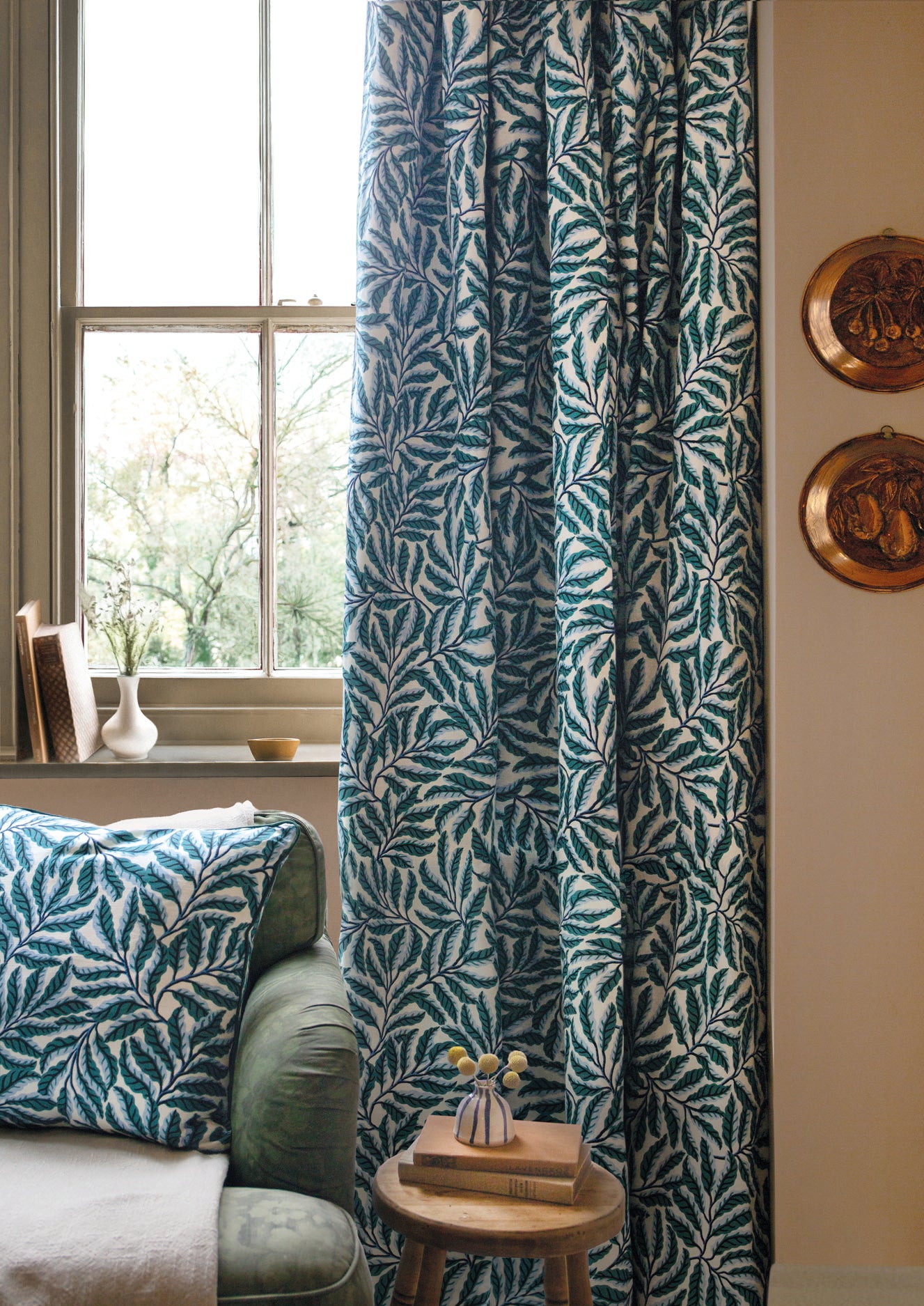 Green leaf-patterned curtain in a room with a couch and decorative items.
