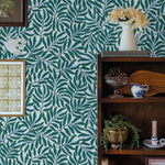 Room interior with green leaf-patterned wallpaper, bookshelf, and decorative items.