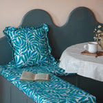Green cushion with leaf pattern on a bench against a beige wall.