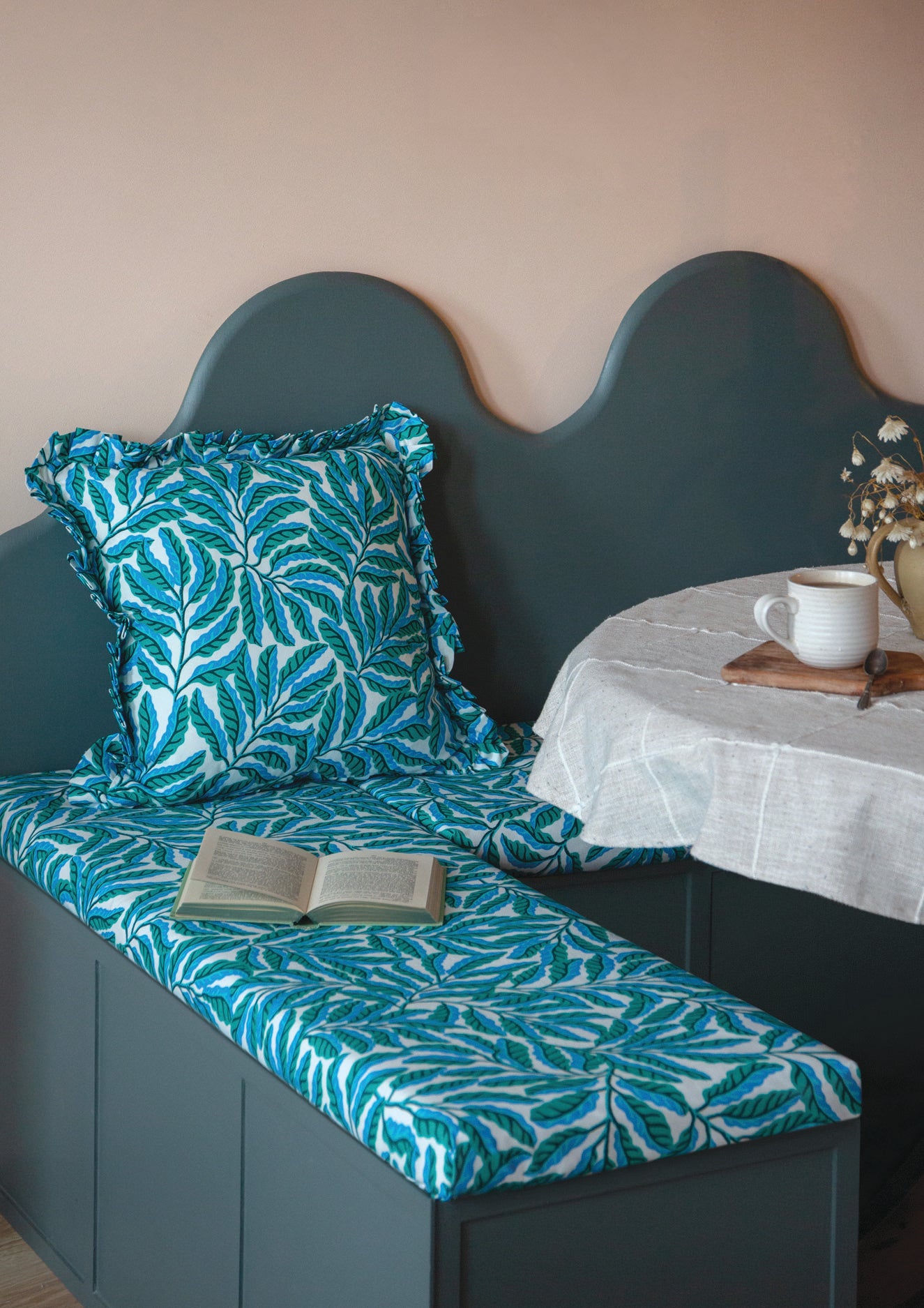 Green cushion with leaf pattern on a bench against a beige wall.