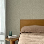 Bed with tan linens and wooden headboard, wooden side table  with white book and green glass, white floor length curtain against a watercolor swirling stripe wallpaper in tonal sage green.