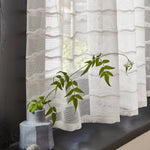 Windowsill with a vase and wildflower with a sheer fabric curtain in a wavy stripe pattern in ivory. 