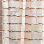 Draped sheer fabric in a wavy stripe pattern in blush with a rust accent.