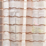 Draped sheer fabric in a wavy stripe pattern in blush with a rust accent.