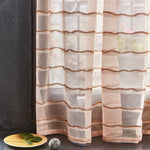 Windowsill with a plate, left and pebble with with a sheer fabric curtain in a wave pattern in blush. 