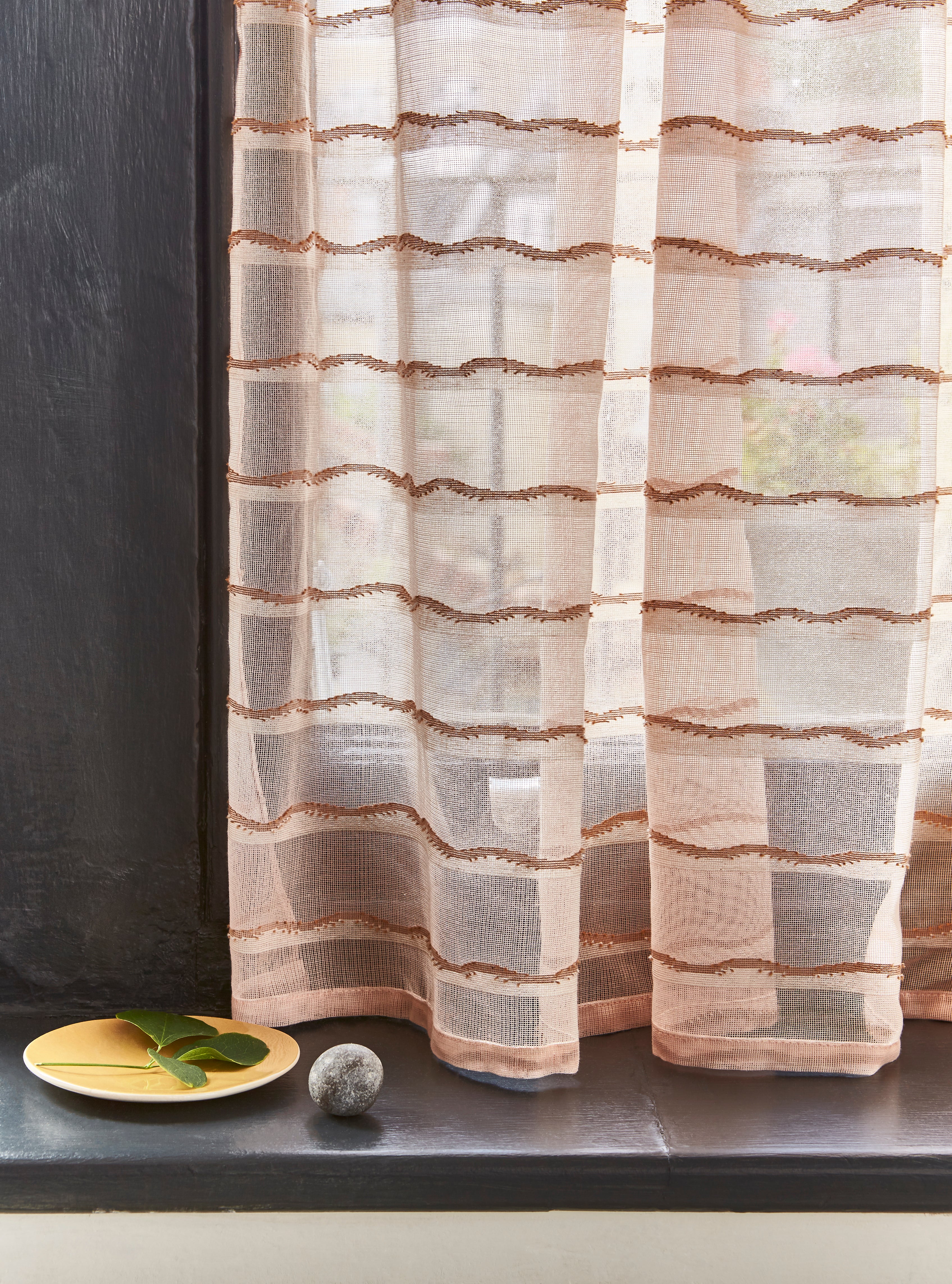 Windowsill with a plate, left and pebble with with a sheer fabric curtain in a wave pattern in blush. 