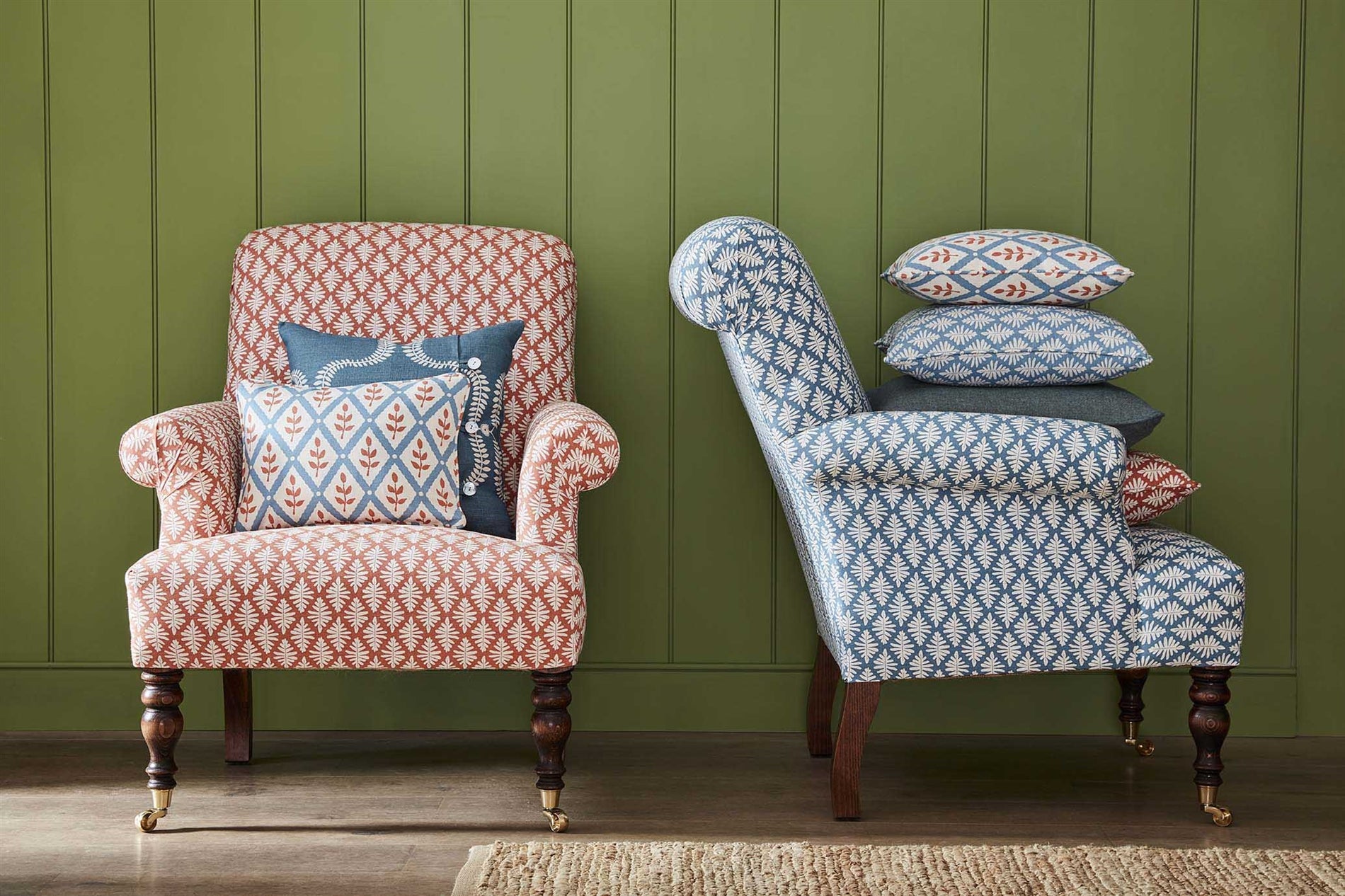 Two armchairs stacked with throw pillows, all in different shades of the same repeating fern leaf print.