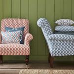 Two armchairs stacked with throw pillows, all in different shades of the same repeating fern leaf print.
