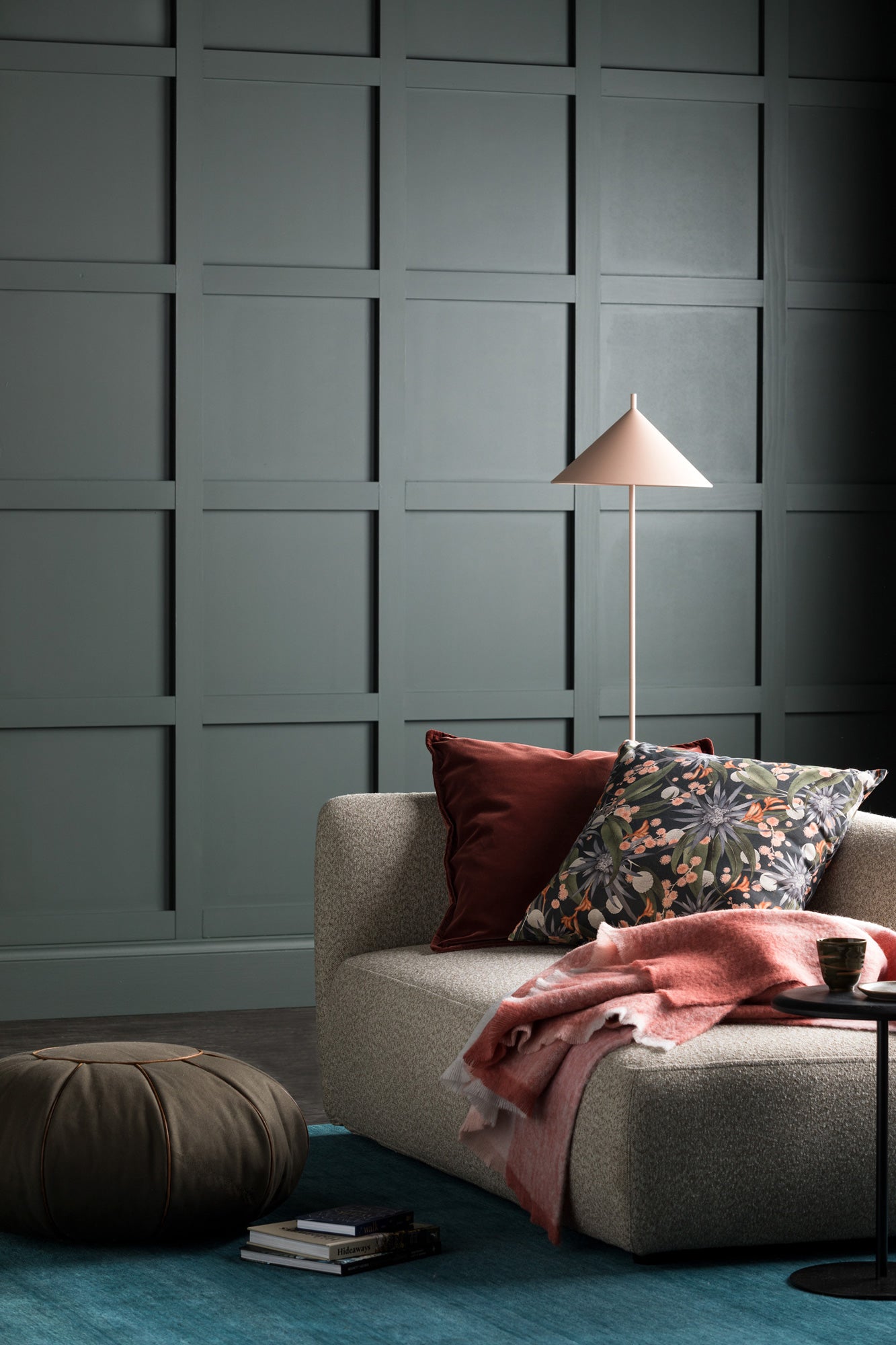 A moody living tableau with dark green walls and a couch stacked in pink and floral throw pillows.