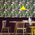 A maximalist dining room with a wall papered in a large-scale botanical print in pink, yellow, green and navy.