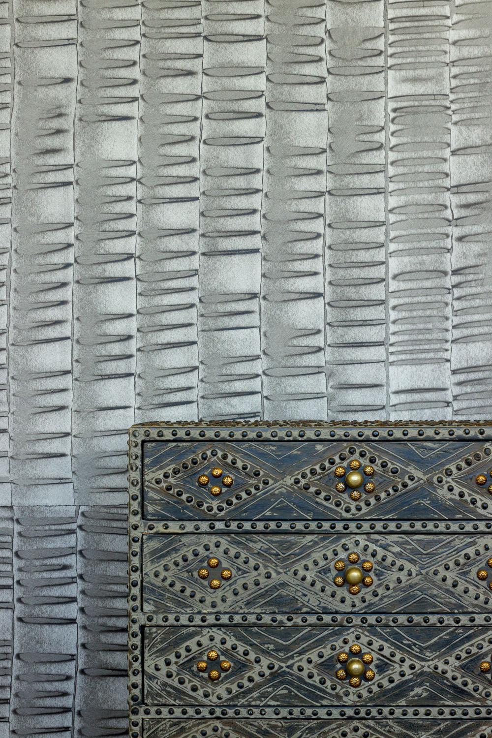 A metal end table stands in front of a wall papered in an undulating ribbon pattern in charcoal.