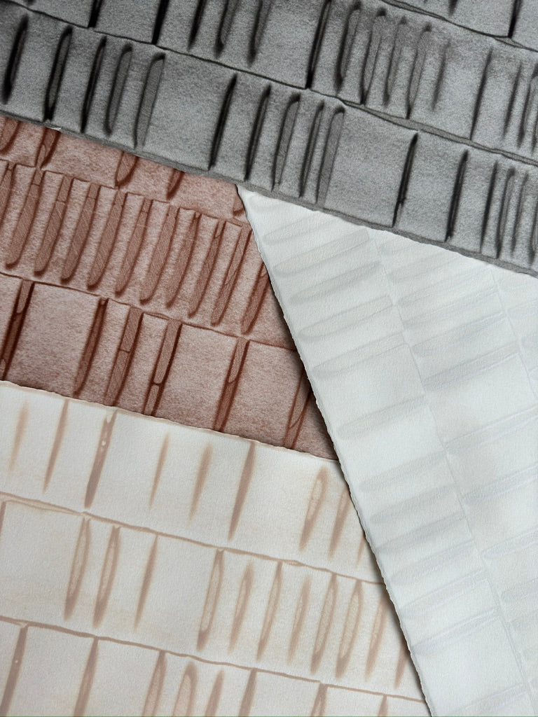Pile of wallpaper swatches with undulating ribbon patterns in peach, copper, ivory and grey.