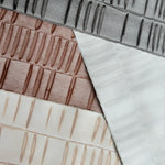 Pile of wallpaper swatches with undulating ribbon patterns in peach, copper, ivory and grey.