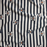 A close-up of a fabric pattern featuring vertical navy blue and off-white stripes with small daisy-like flowers in navy, white, and orange.