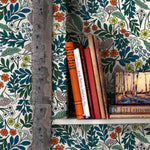 A bookshelf installed on a wall papered in a small-scale floral print in blue, green, orange and white.
