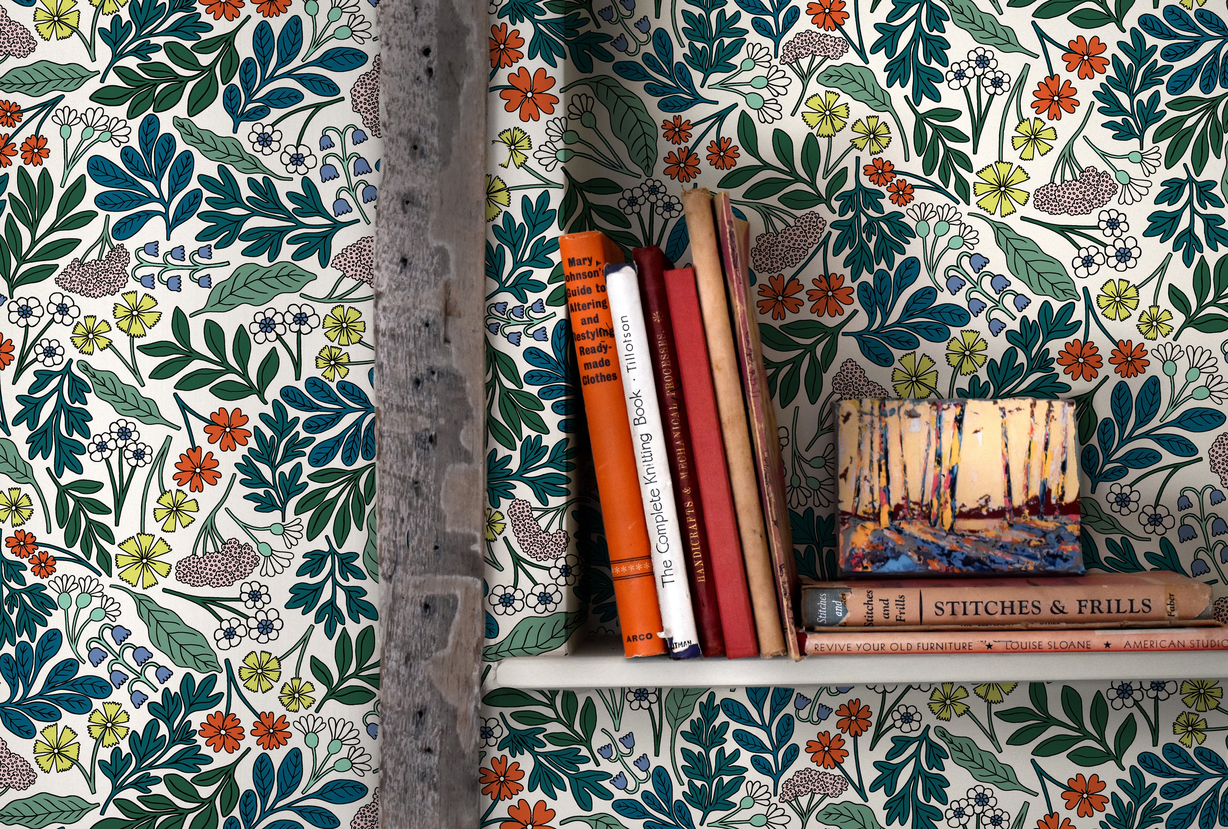 A bookshelf installed on a wall papered in a small-scale floral print in blue, green, orange and white.