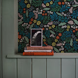 A stack of books leans against a wall papered in a small-scale floral print in blue, green, orange and black.