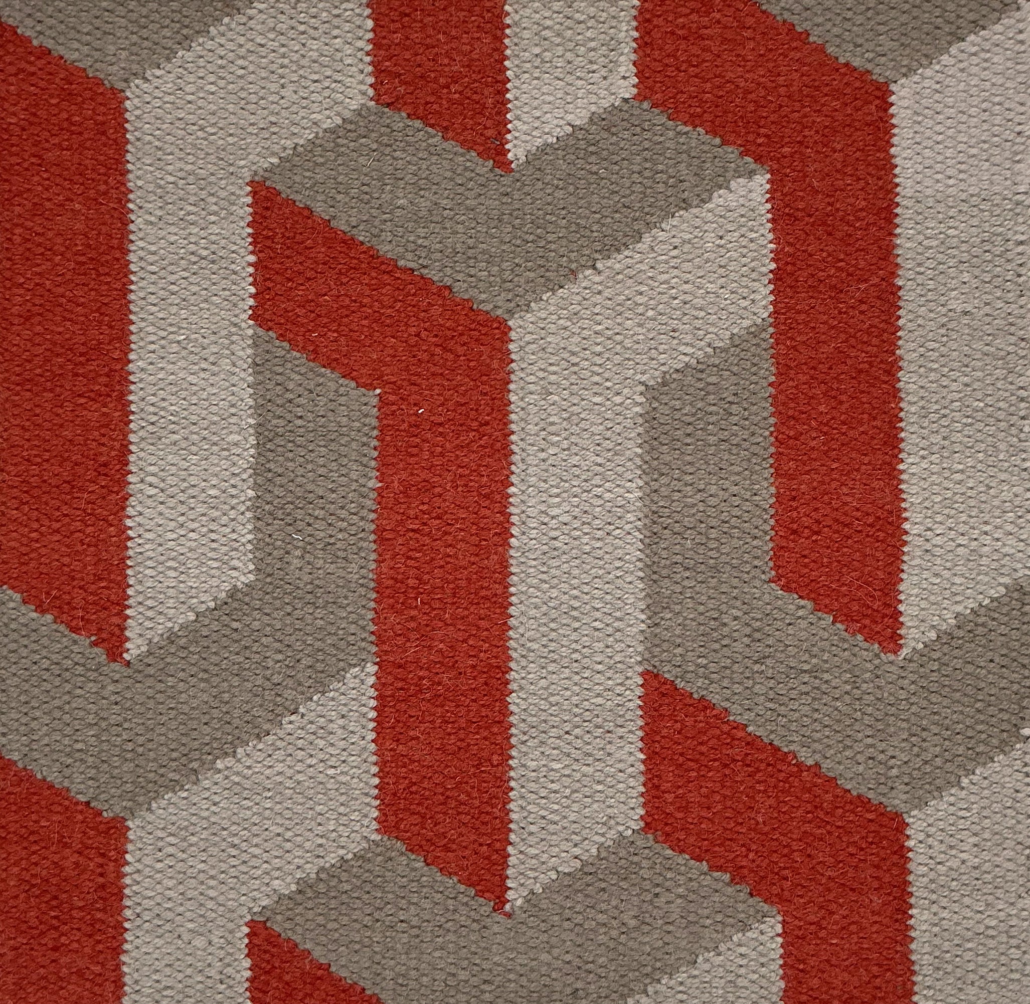 Close-up of a geometric patterned rug with red and gray colors.