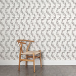 Wooden chair against wallpaper with stripe pattern of stylized ink black leaves on a cream background
