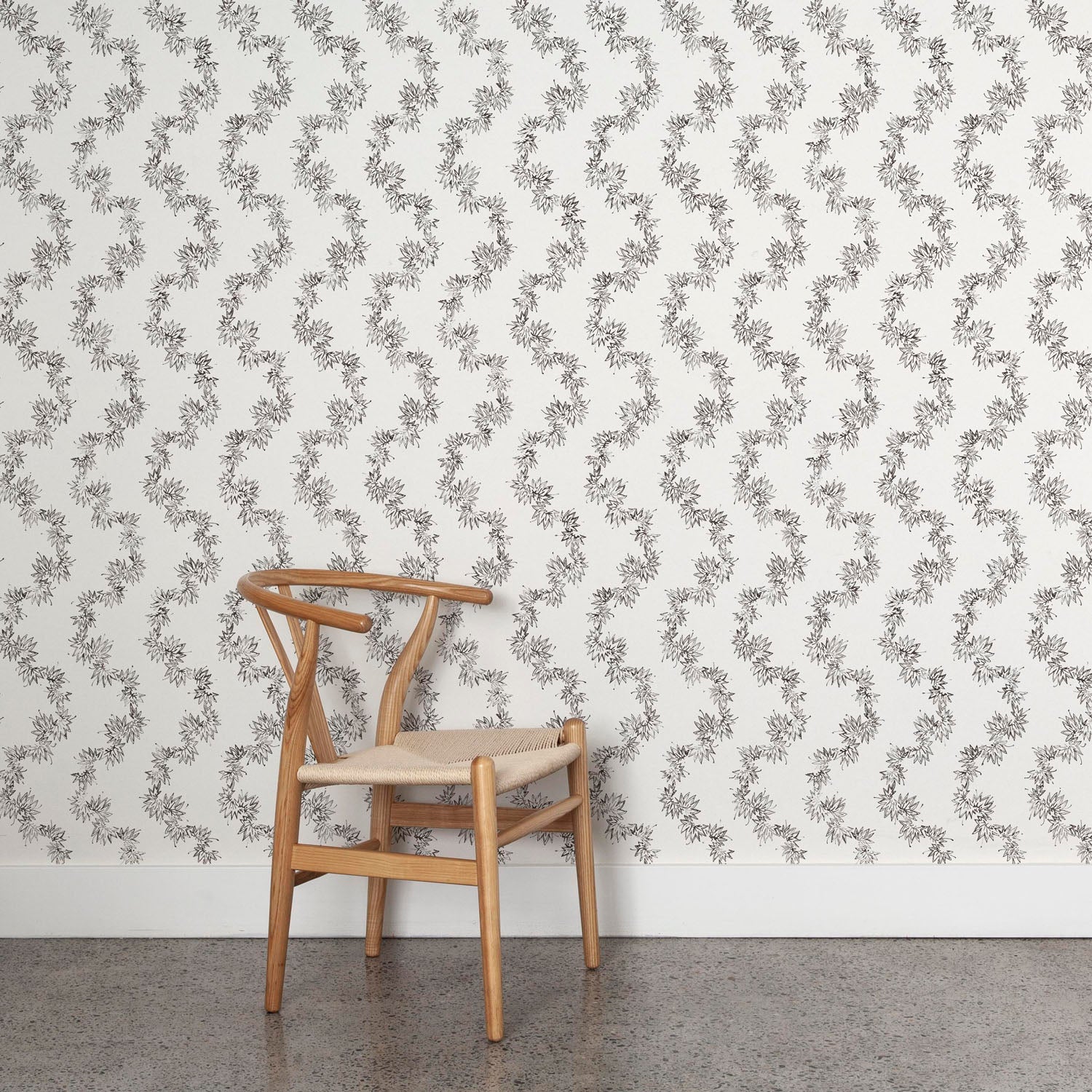 Wooden chair against wallpaper with stripe pattern of stylized ink black leaves on a cream background