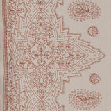 Detail of fabric in a dense paisley border print in rust on a tan field.